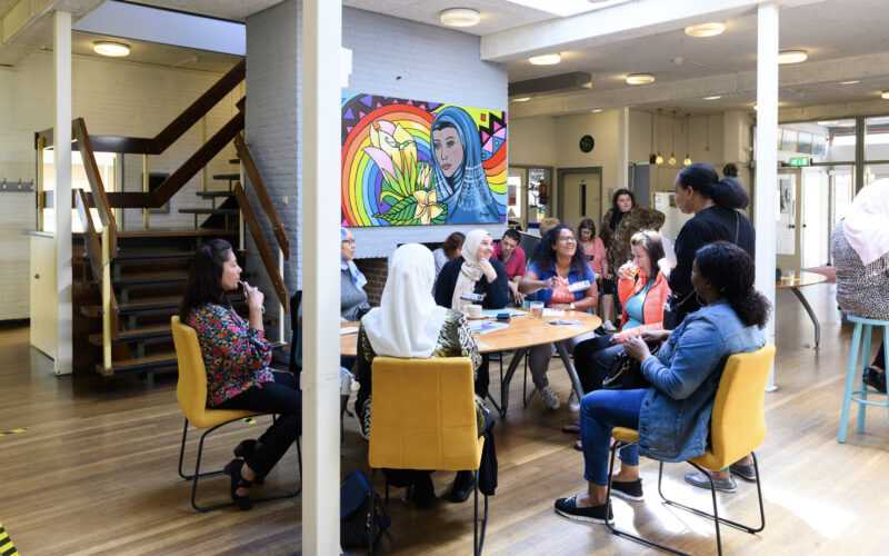 Groep volwassenen in zaal met meerdere tafel gezellig met elkaar in gesprek