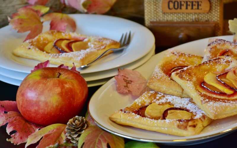 Appel op de voorgrond met daarachter gebaksbordjes met appelgebakjes