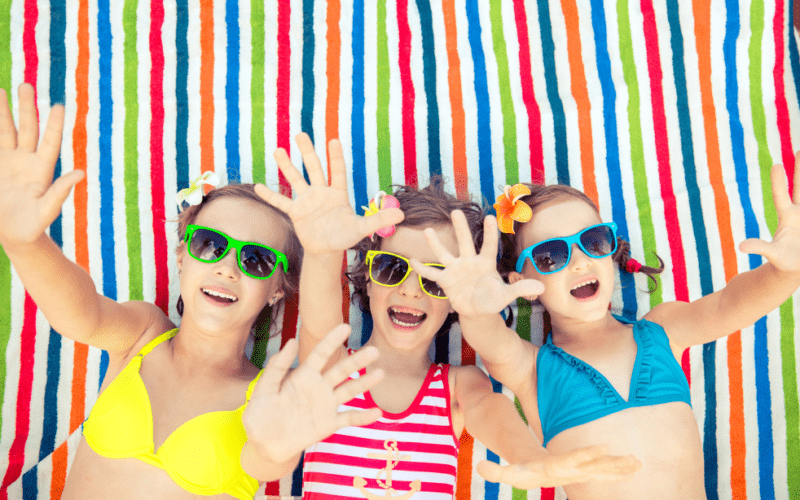 drie kinderen op gekleurd badlaken met zonnebrillen op