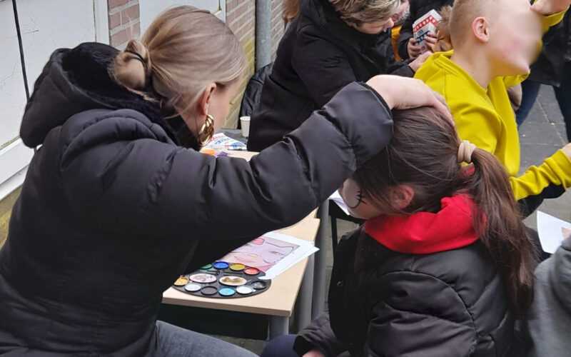 moeder schminkt basisschoolkind buiten op het plein